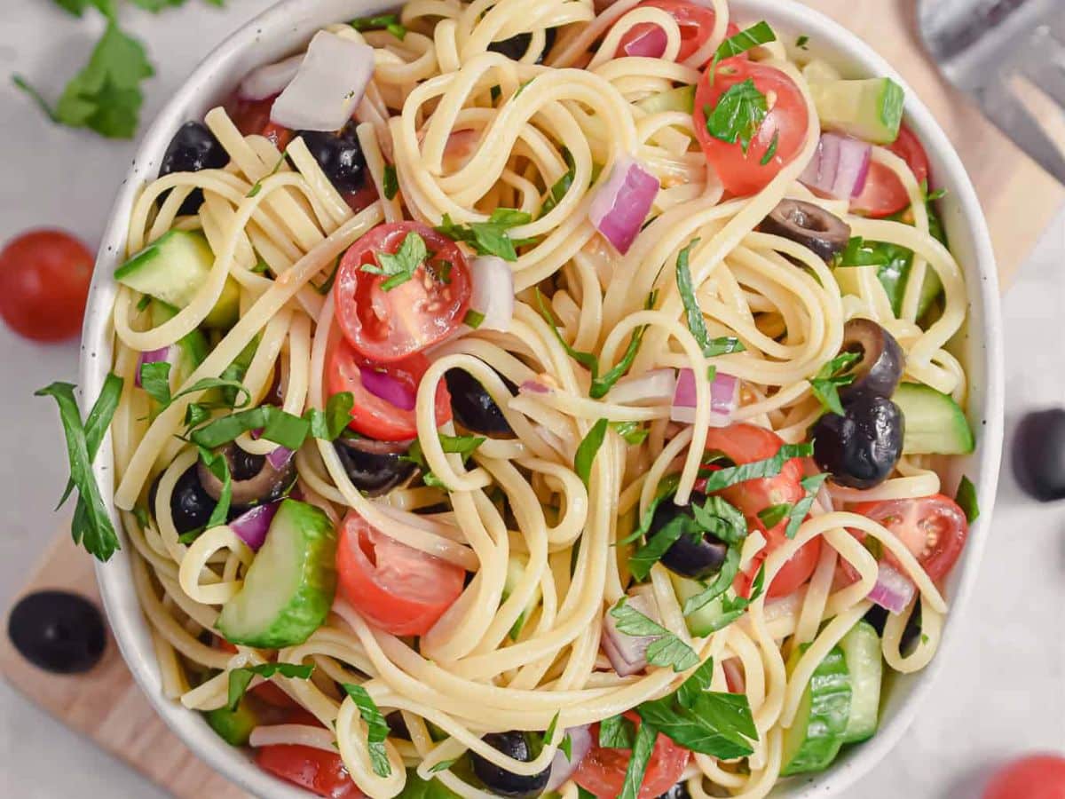 A bowl of pasta salad with olives, tomatoes and black olives.