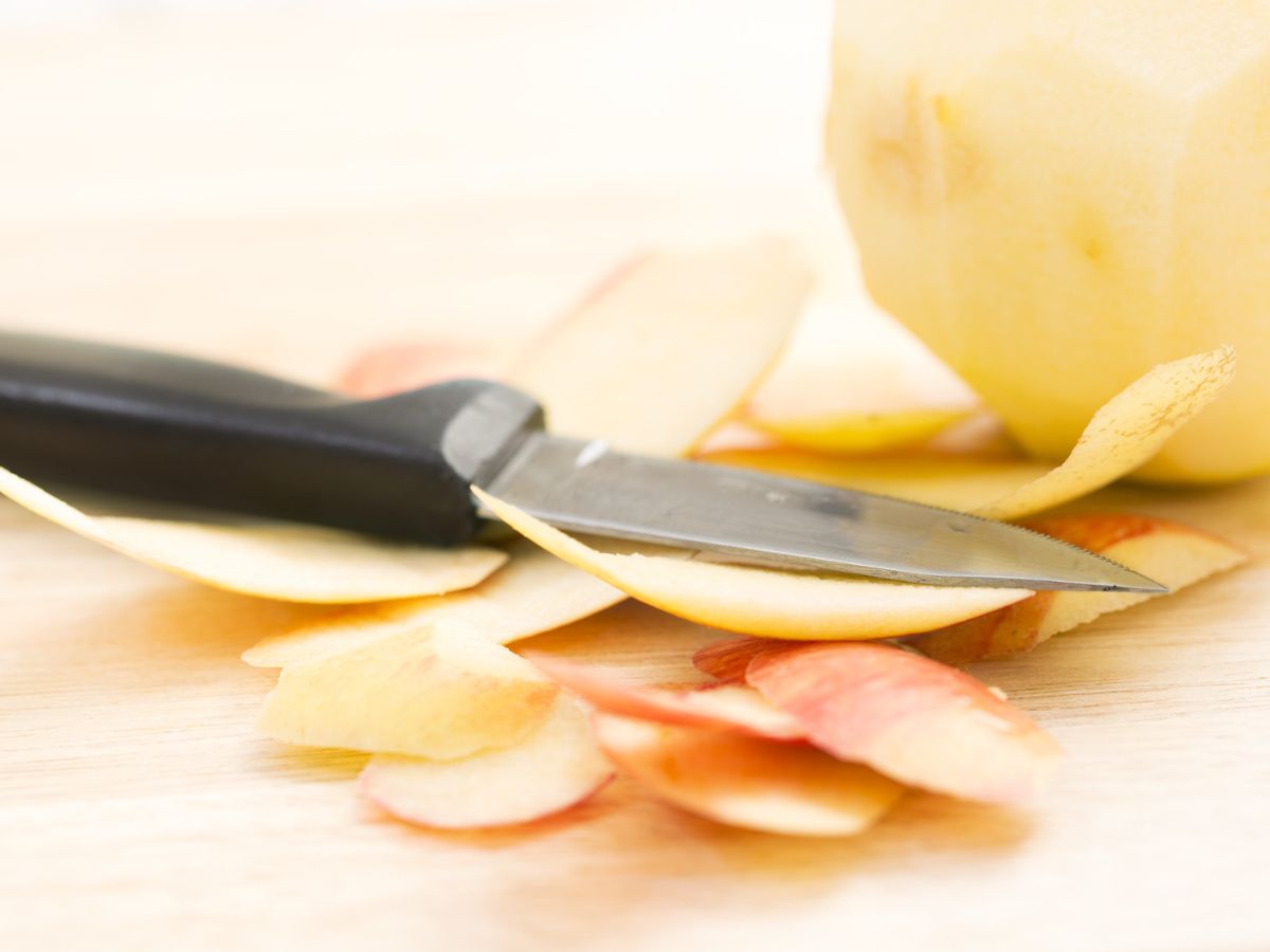 A paring knife by an apple and apple peels.