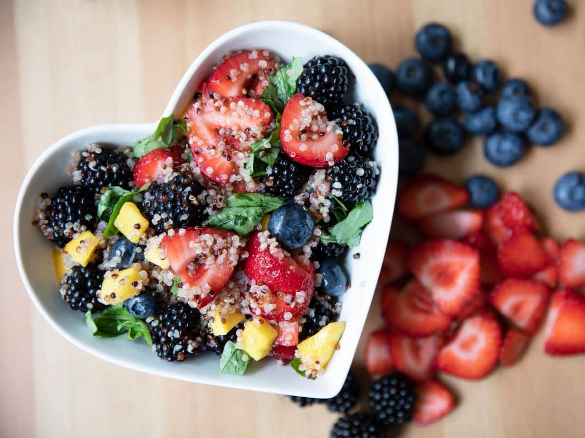 A heart shaped bowl of a quinoa salad made with fresh fruits.