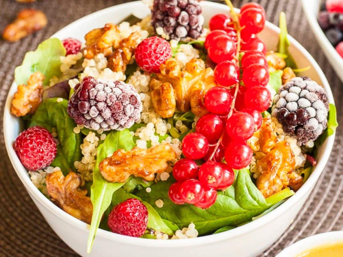 A bowl of quinoa salad topped with fresh berries and candied nuts.