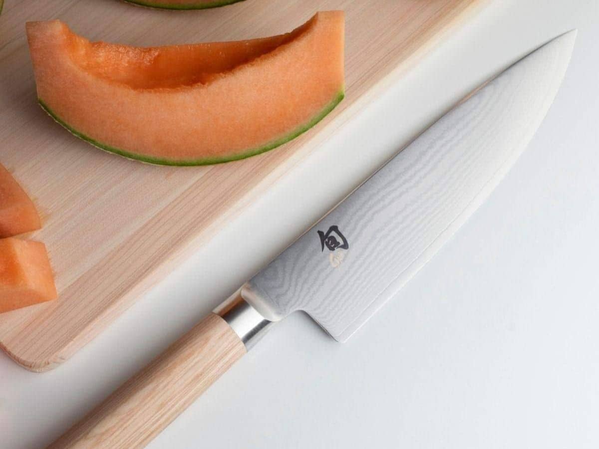 A knife with a slice of canteloupe on a cutting board.