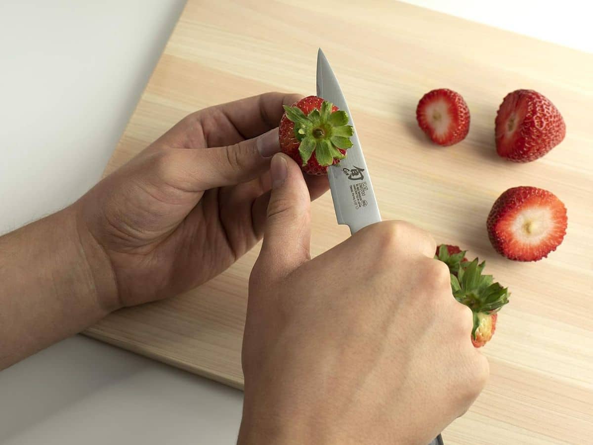 A person cutting strawberries with a paring knife.