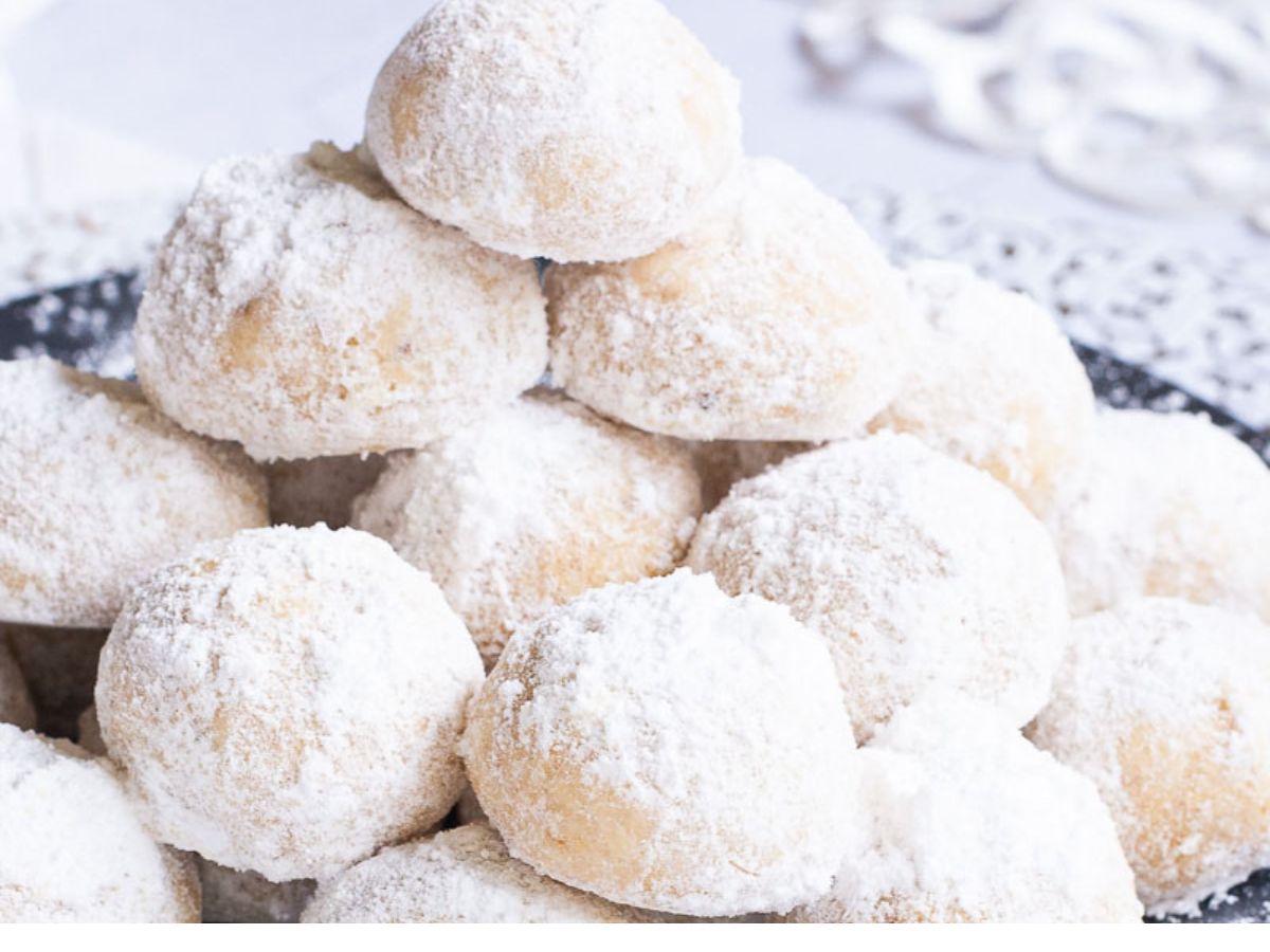 A pile of powdered sugar cookies on a plate.