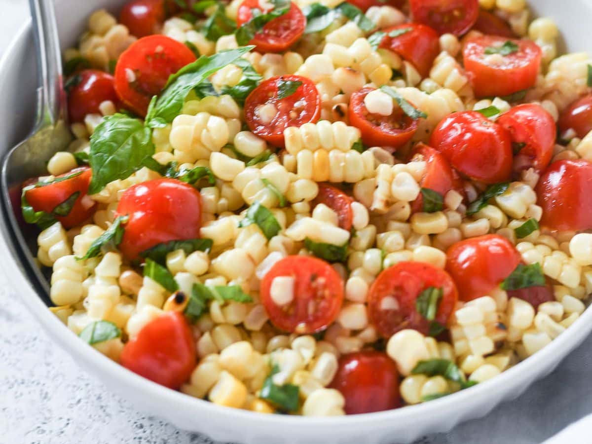 Corn salad with tomatoes and basil in a white bowl.