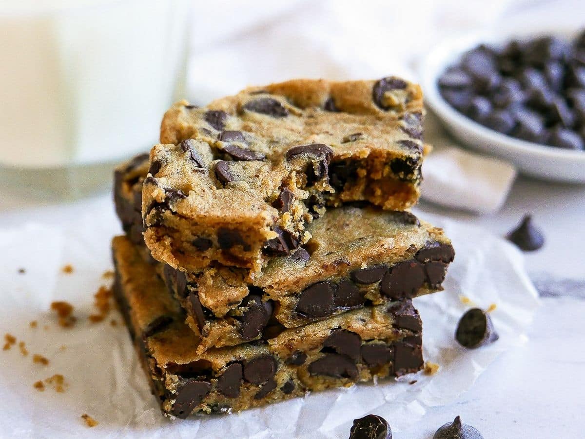 A stack of chocolate chip cookie bars next to a glass of milk.