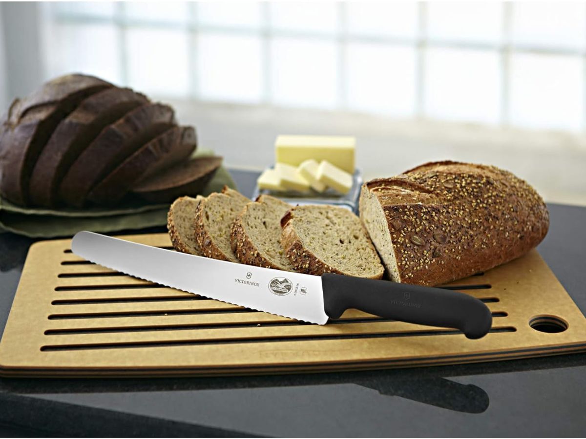A Victorinox serrated bread knife on a cutting board next to a loaf of bread.
