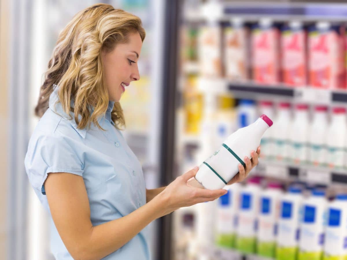 A woman is looking at a bottle of milk in a store.