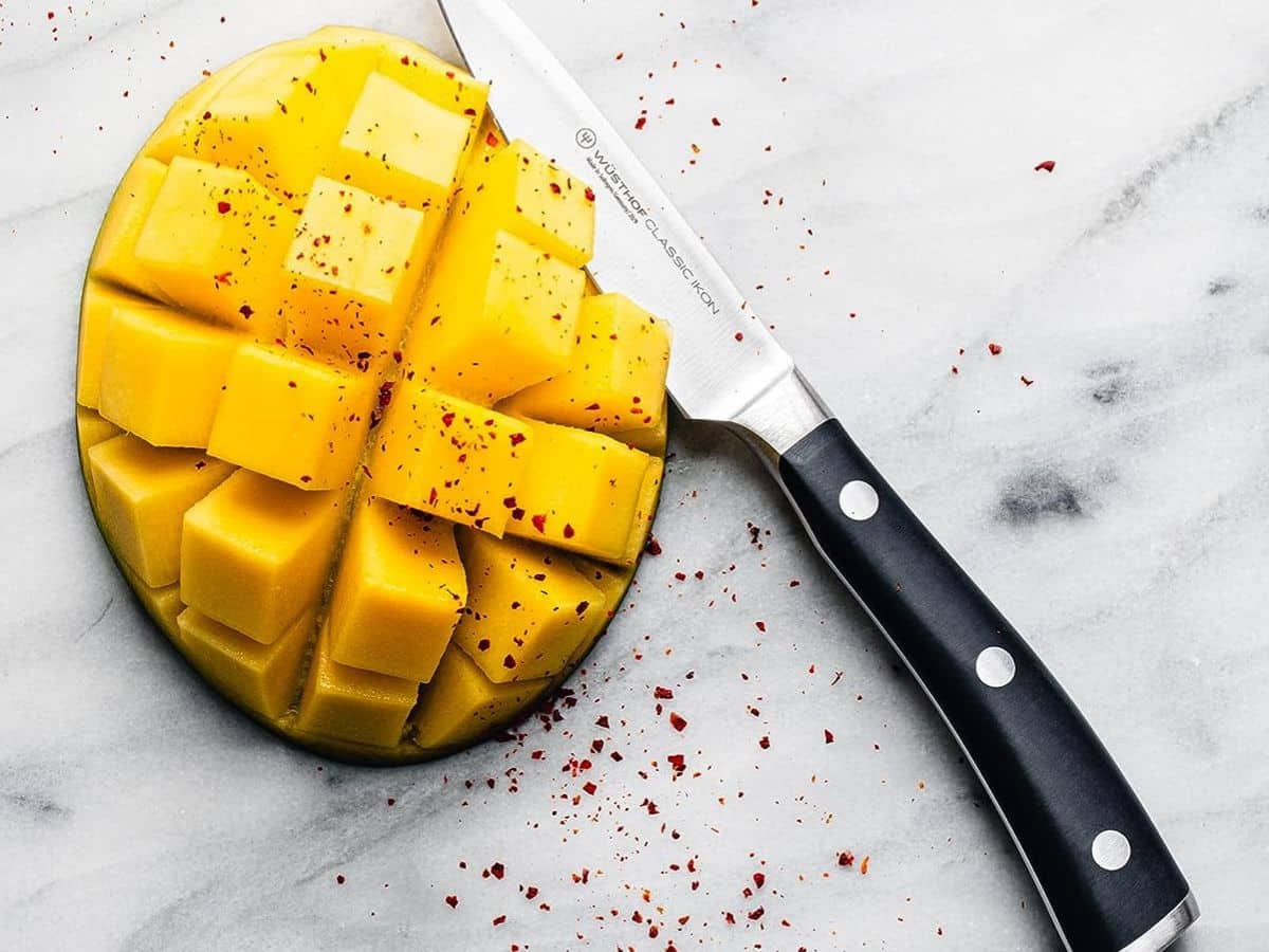 A slice of mango with a knife next to it.