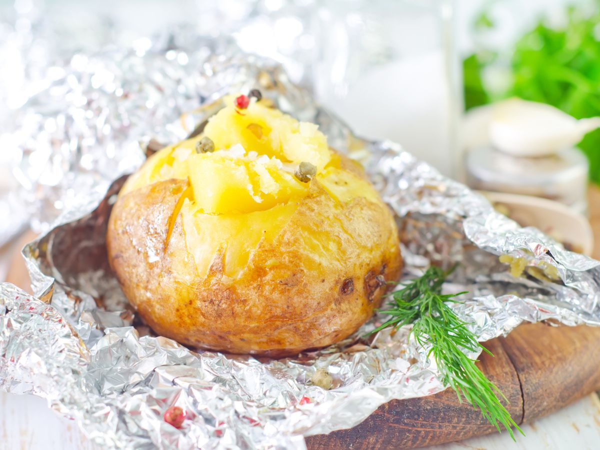 A potato wrapped in foil on a wooden table.