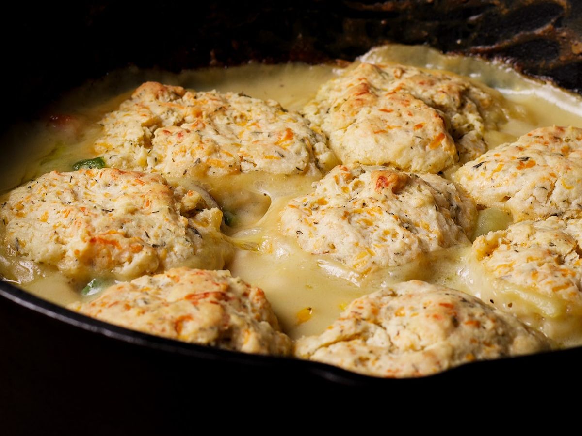 A cast iron skillet of turkey pot pie topped with cheddar biscuits.