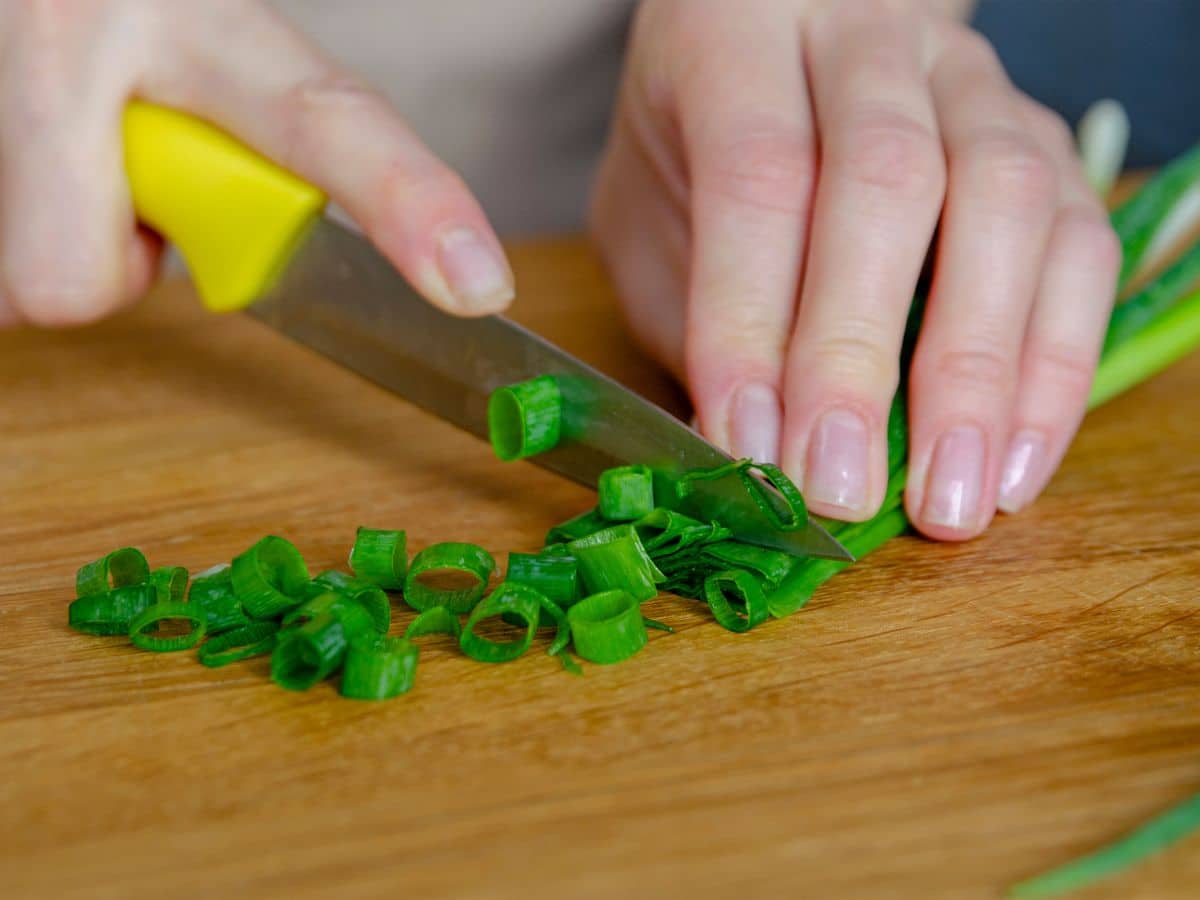 A person slicing green onions on a cutting board.