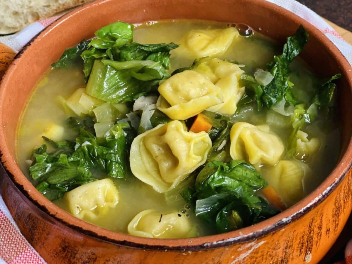 A bowl of turkey tortellini soup with greens and bread.