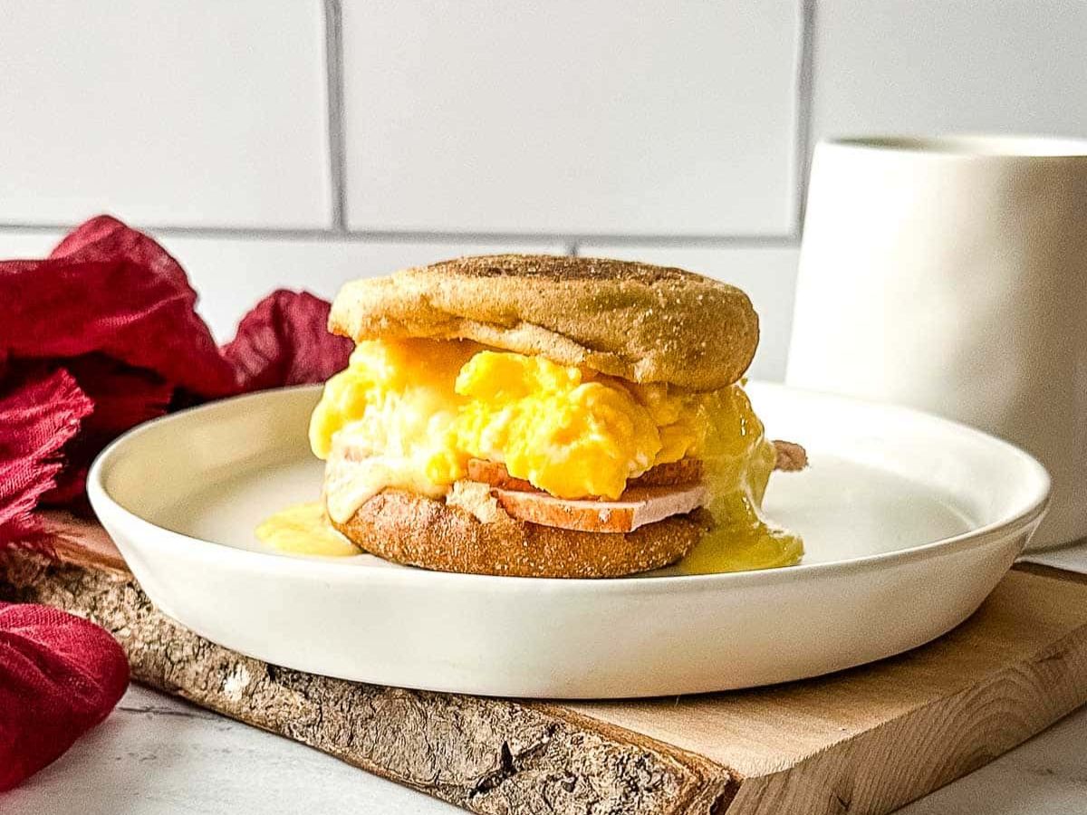 A breakfast sandwich on a plate next to a cup of coffee.