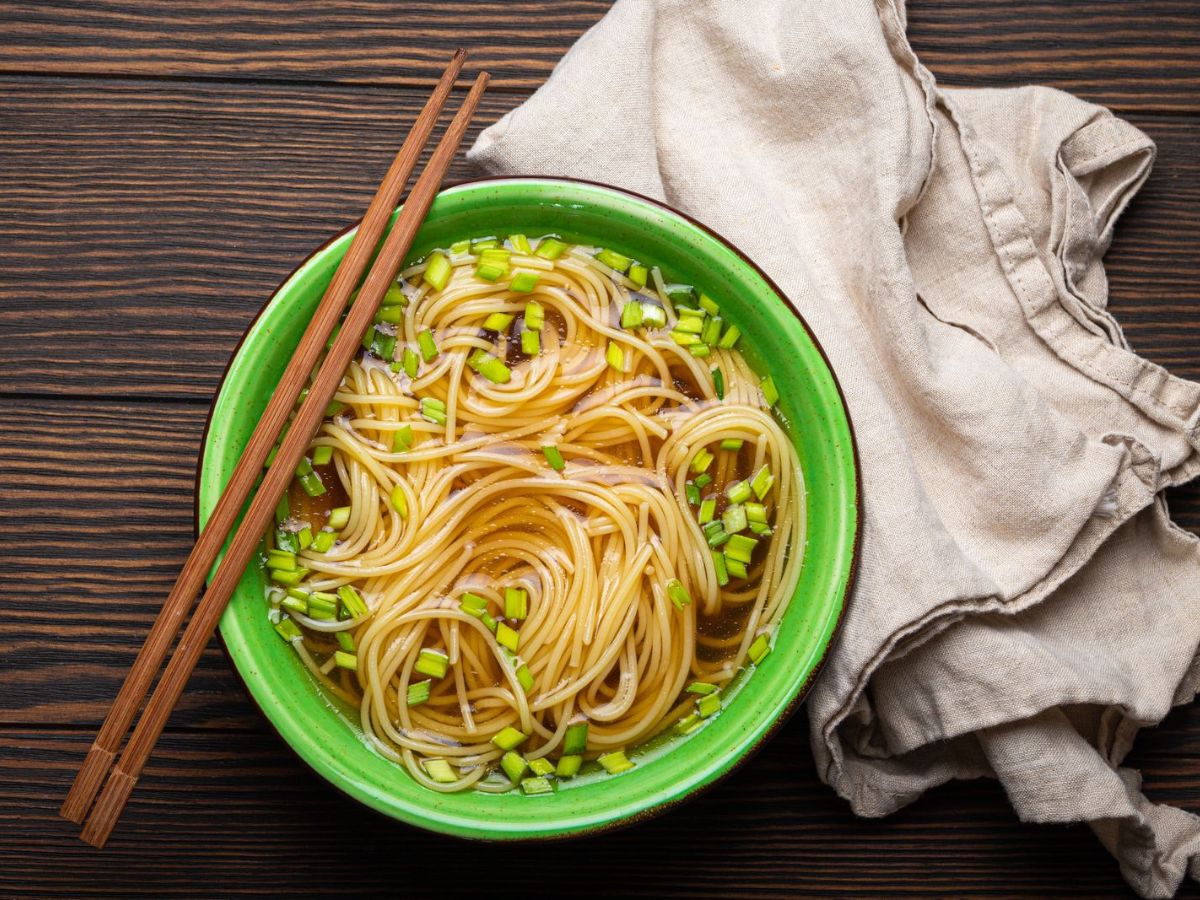 A bowl of noodles with homemade chicken broth and chopsticks on a wooden table.