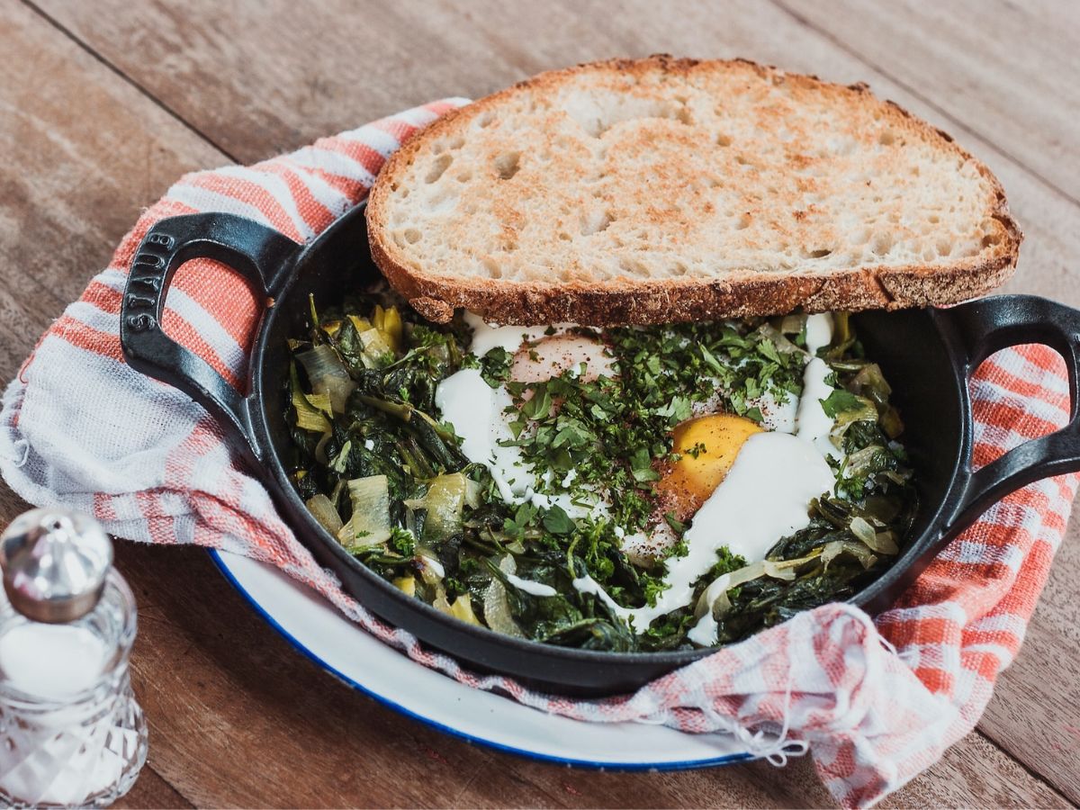 A cast iron skillet with eggs and greens on a table.
