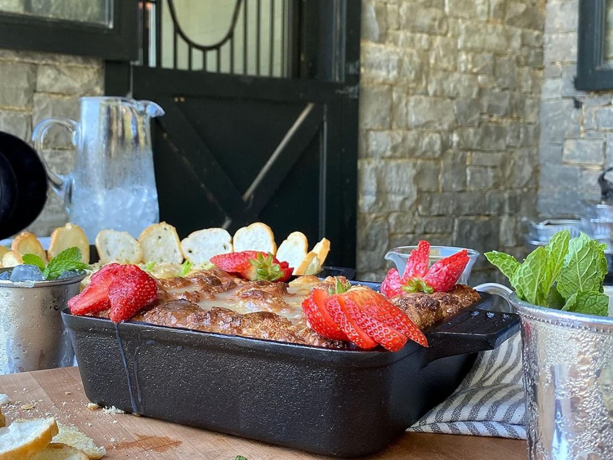 A cast iron baking dish with French toast topped with strawberries on a wooden table.