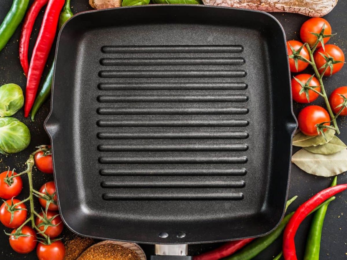 An empty cast iron grill pan surrounded by tomatoes, peppers and other vegetables.