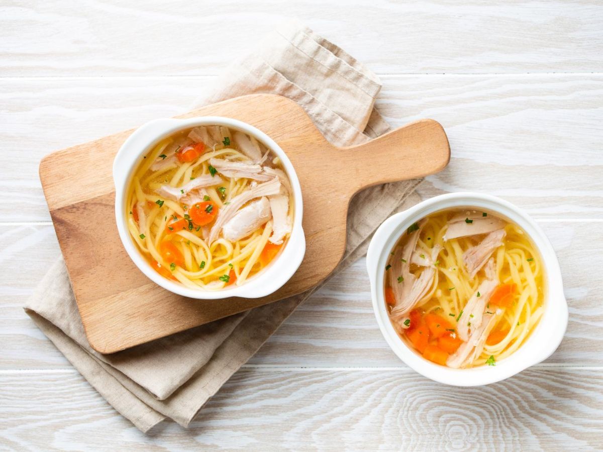 Two bowls of chicken noodle soup made with homemade chicken broth on a wooden cutting board.