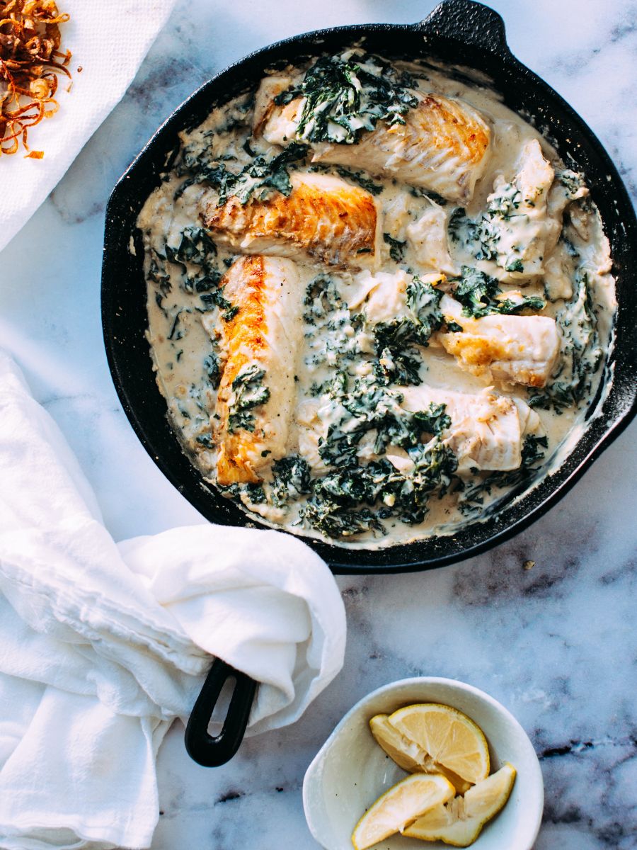 A cast iron skillet filled with fish and spinach.