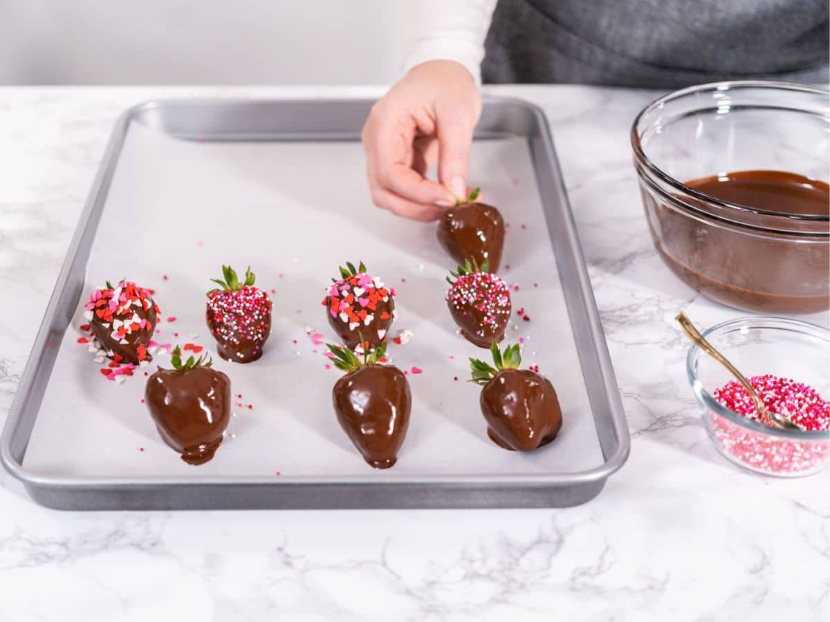 A woman dipping fresh strawberries into melted chocolate.