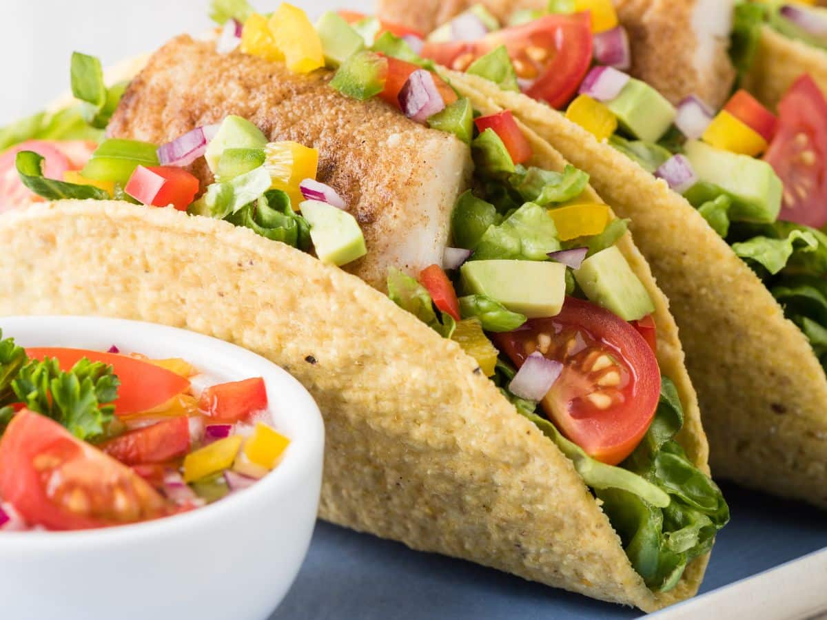 Two fish tacos filled with fresh vegetables and topped with zesty salsa, all beautifully presented on a plate.