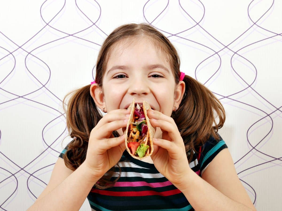 A little girl is enjoying a delicious taco in front of a white background.
