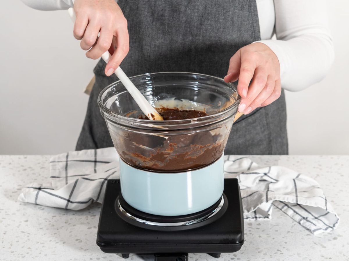 A woman melting chocolate using a cooktop and double boiler.