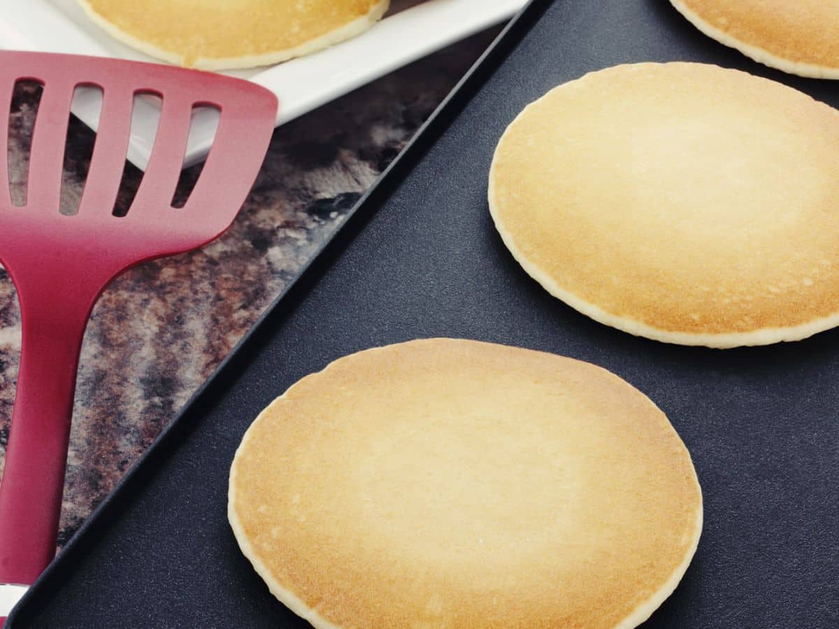 Pancakes cooking on a cast iron griddle.