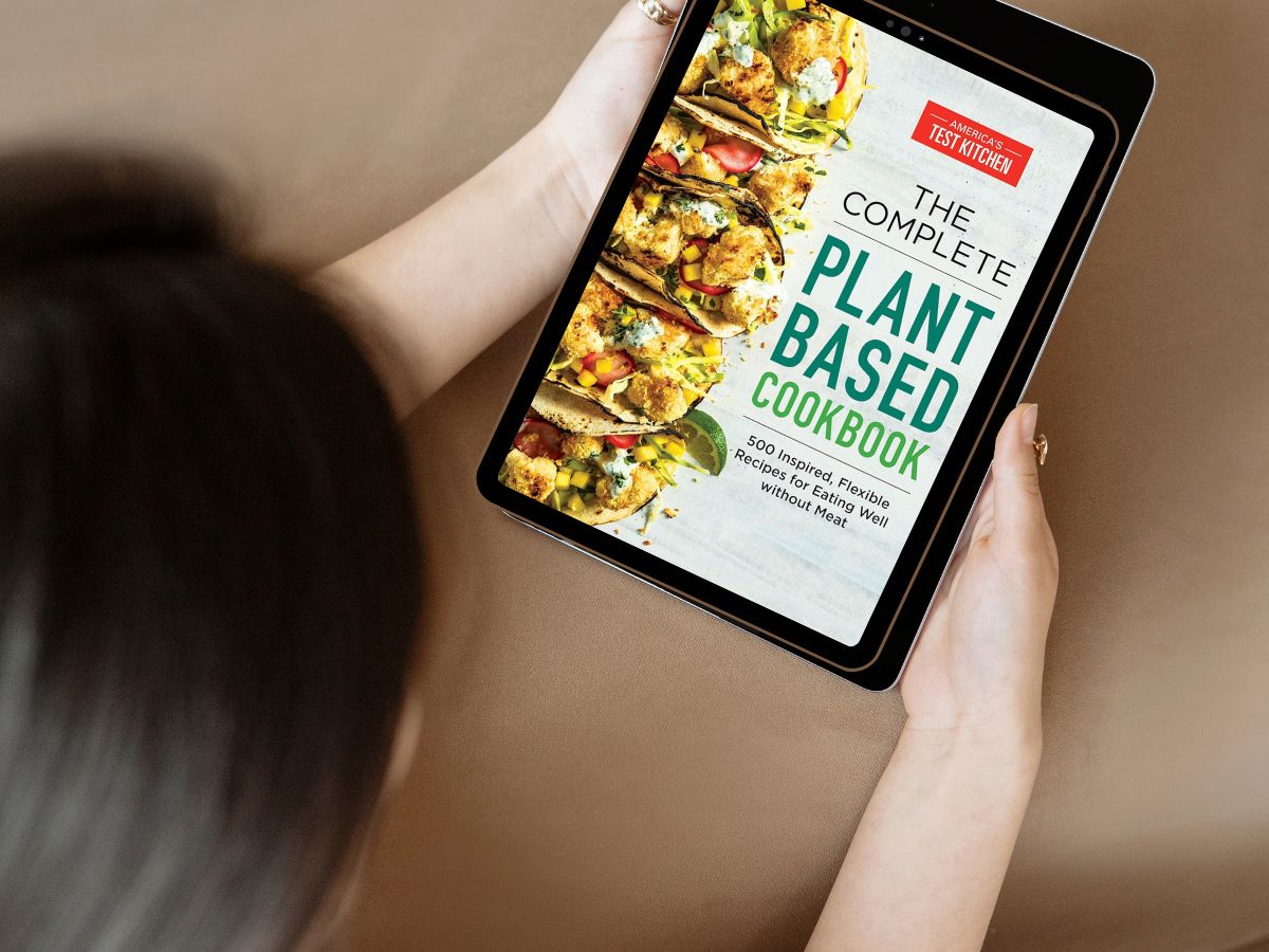 A woman looking at The Complete Plant Based Cookbook on a tablet.