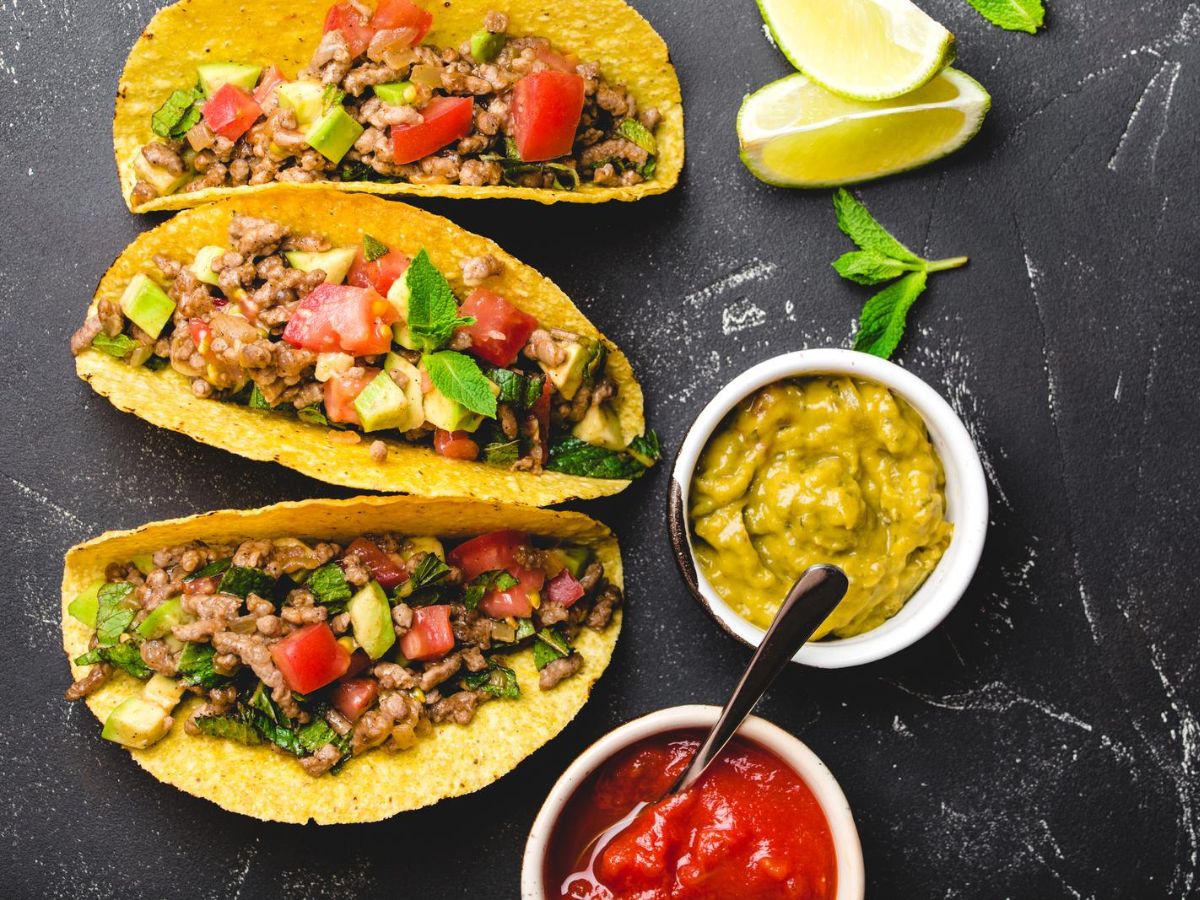 Three traditional Mexican tacos with guacamole and salsa.