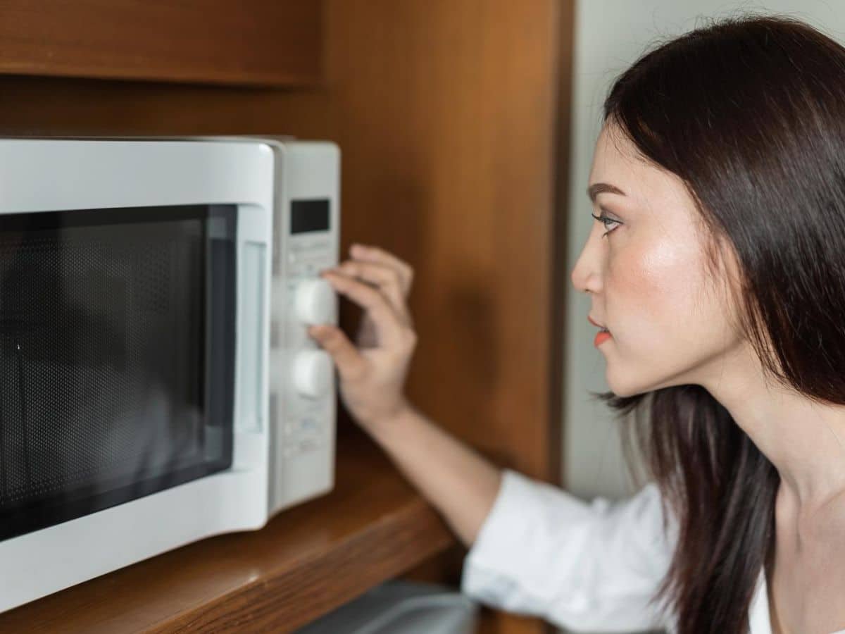 A woman using a microwave oven to melt chocolate.