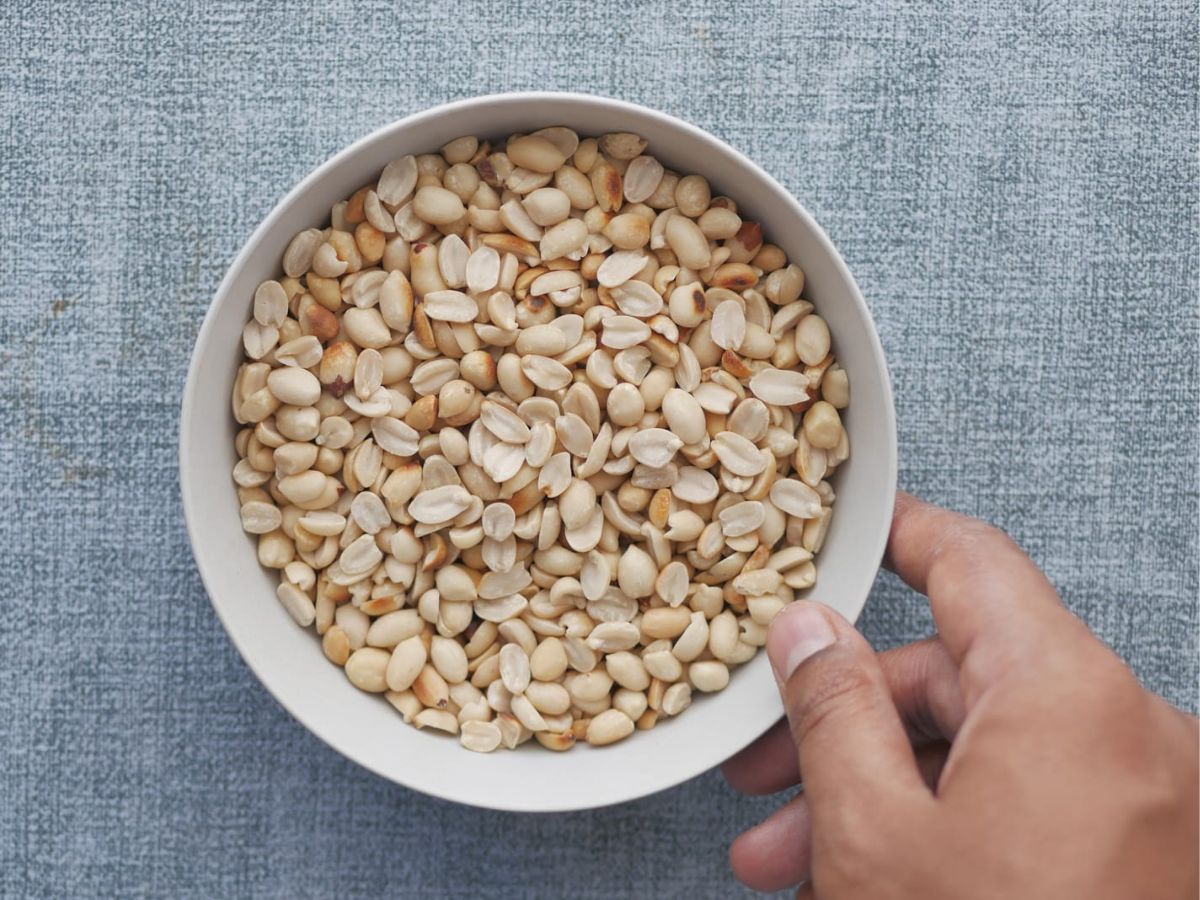 A hand holding a bowl of peanuts, ready to make homemade peanut butter.