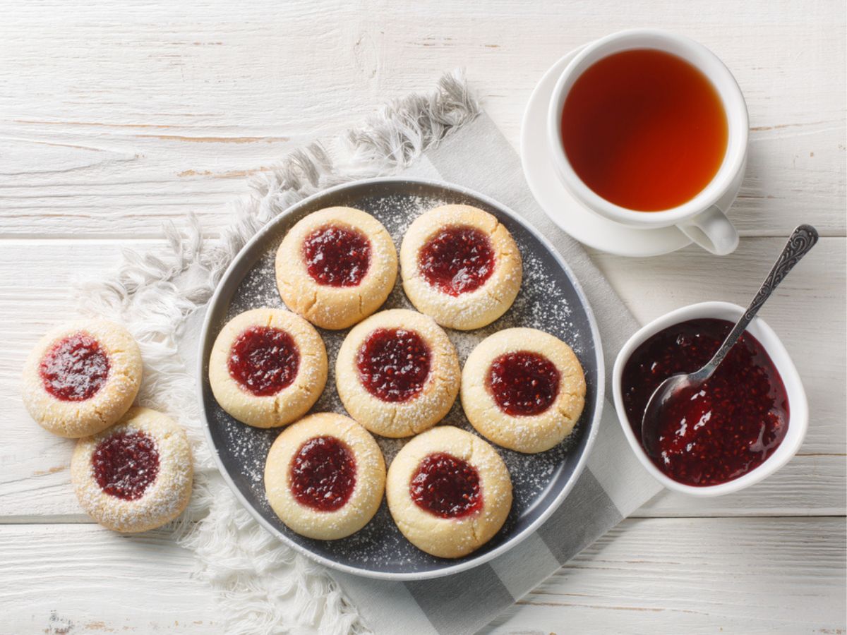 A plate of jam-filled vegan thumbprint cookies with a cup of tea.