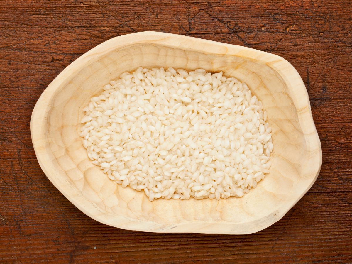 A bowl of uncooked arborio rice on a wooden table.