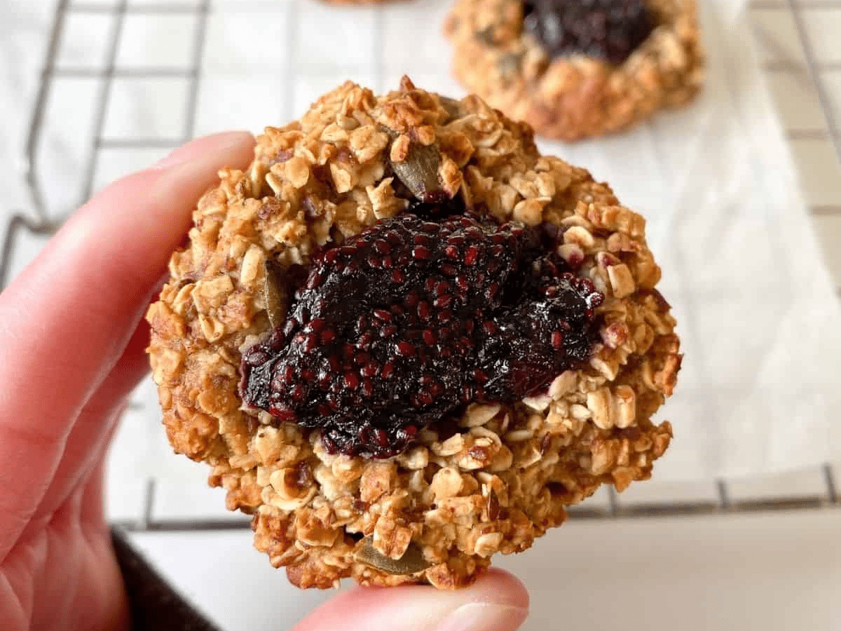 A person holding a vegan thumbprint cookie with jam on it.