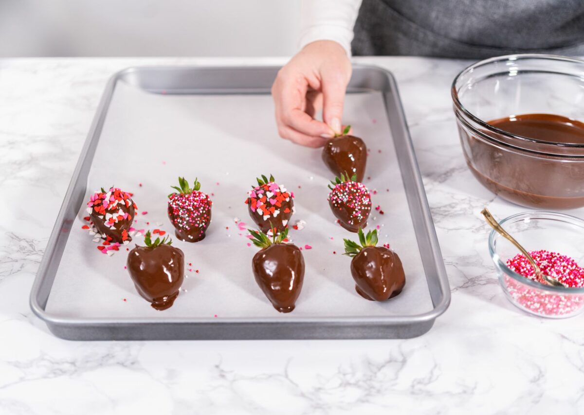 A person making chocolate covered strawberries on a baking sheet.