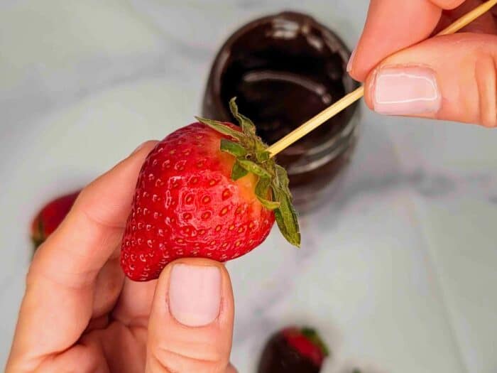 A person carefully inserting a toothpick into a fresh strawberry.