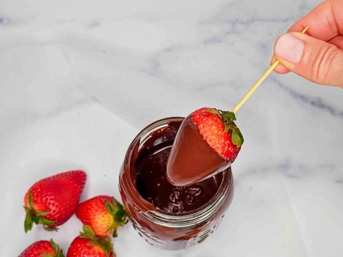 A person is dipping a strawberry into a jar of chocolate to make chocolate covered strawberries.