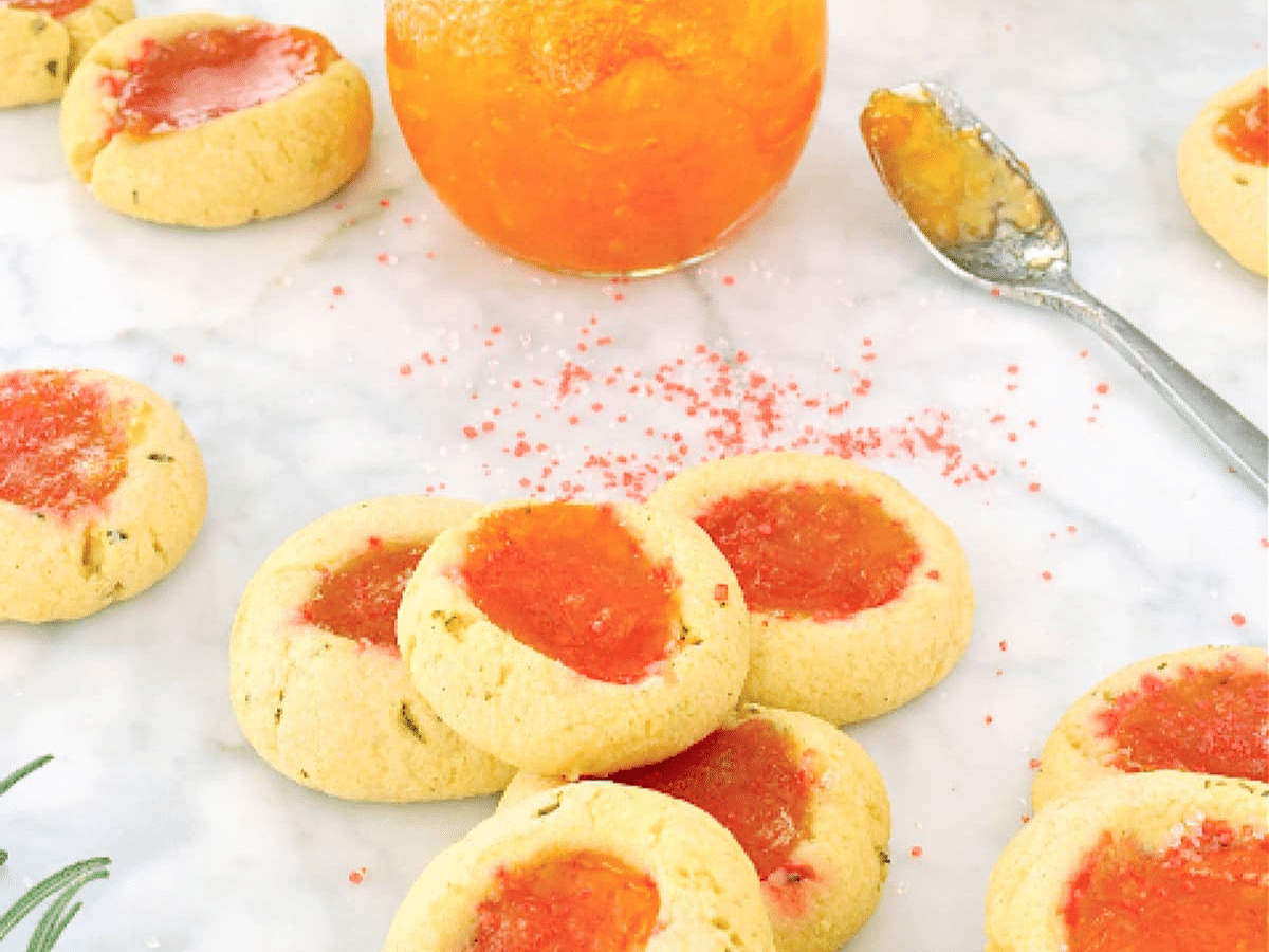 A tray of vegan thumbprint cookies with orange jam and a jar.