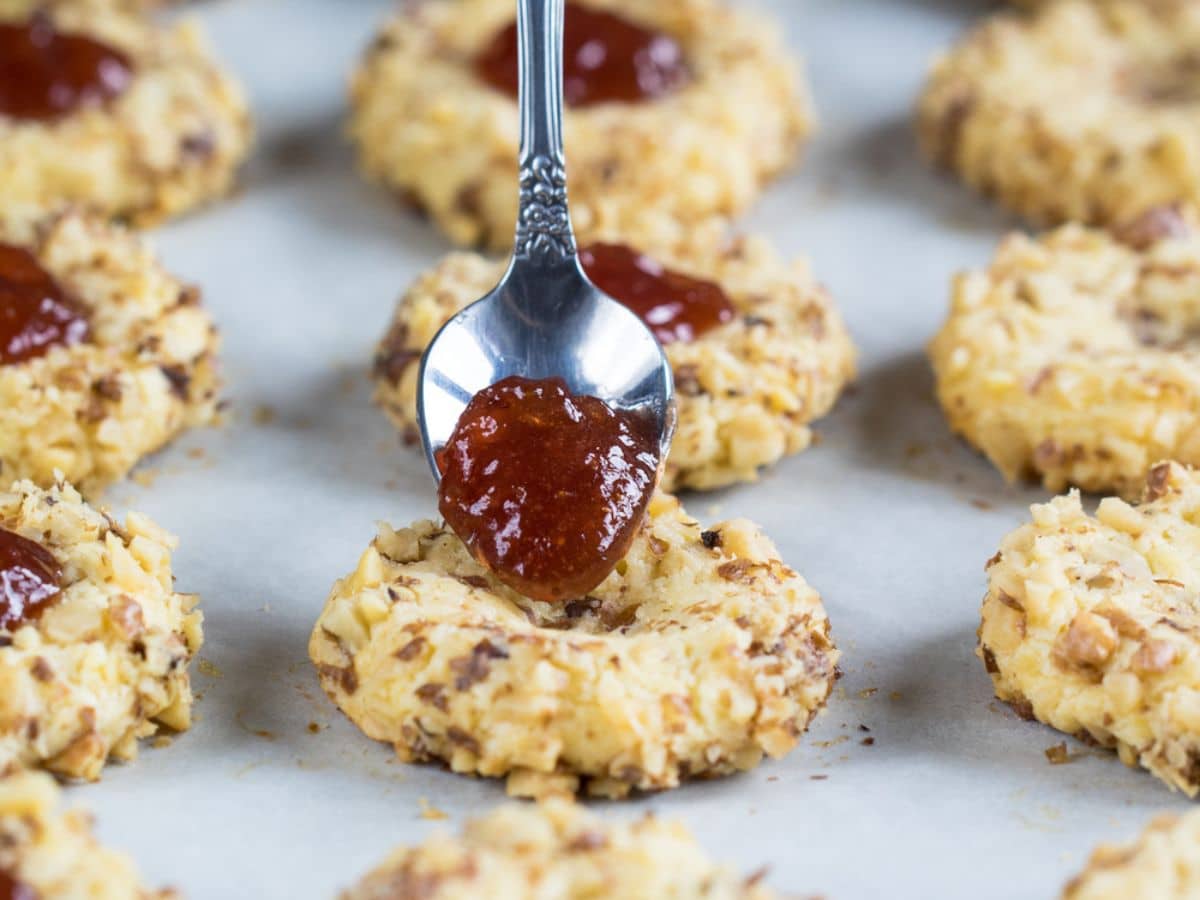 A spoon is being used to dip a vegan thumbprint cookie in jam.