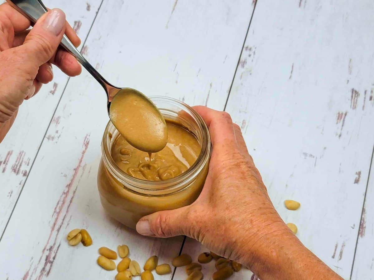A person spooning homemade peanut butter into a jar.