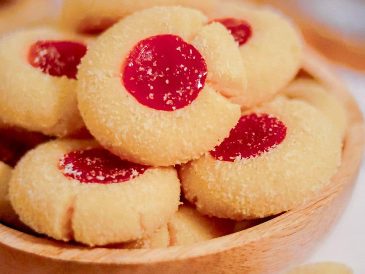 A wooden bowl filled with vegan thumbprint cookies topped with jam.