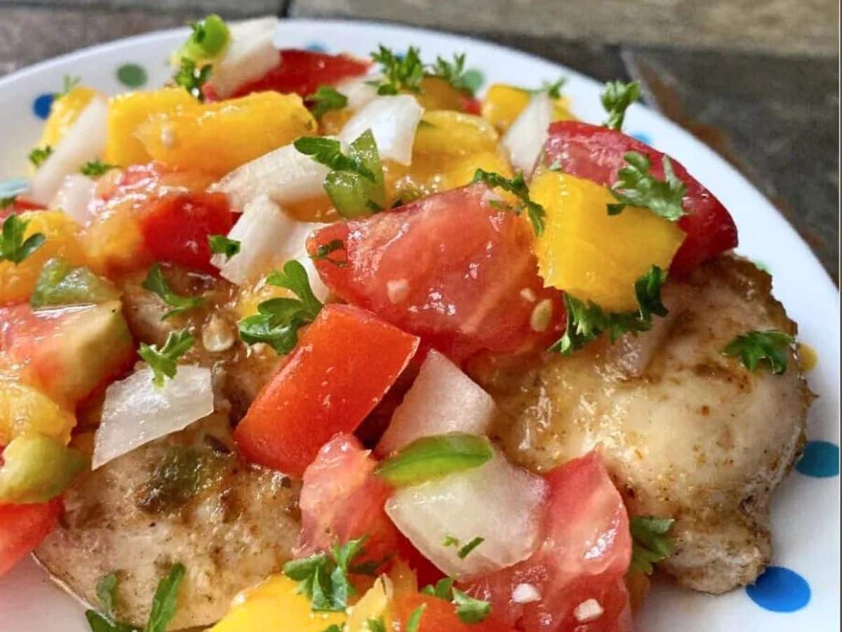 Grilled chicken topped with a colorful salsa of diced tomatoes, mango, and onions, garnished with fresh parsley.