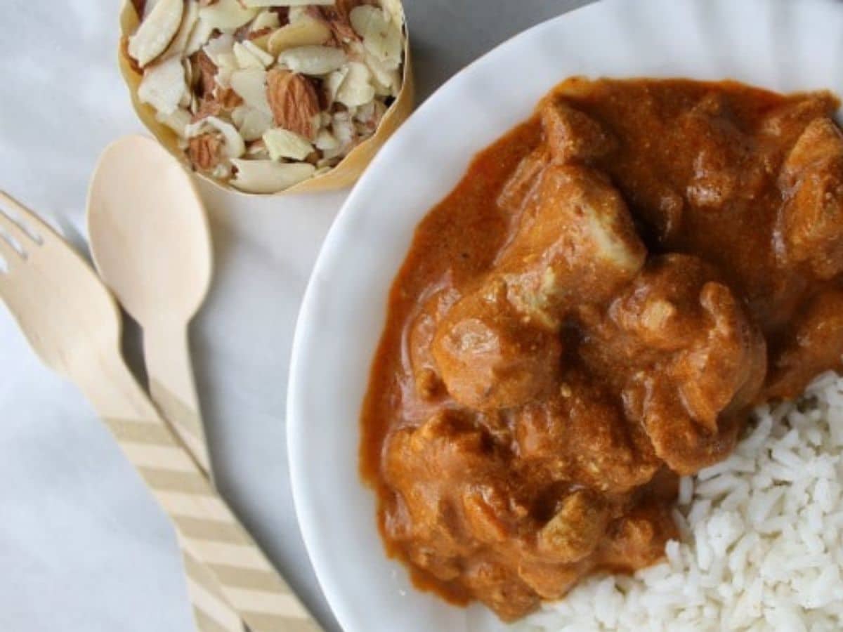A plate of chicken tikka masala served with white rice, accompanied by a bowl of mixed nuts on a white tablecloth.