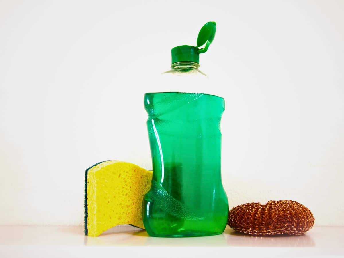 A green bottle of cleaning liquid next to a sponge and scrubber.
