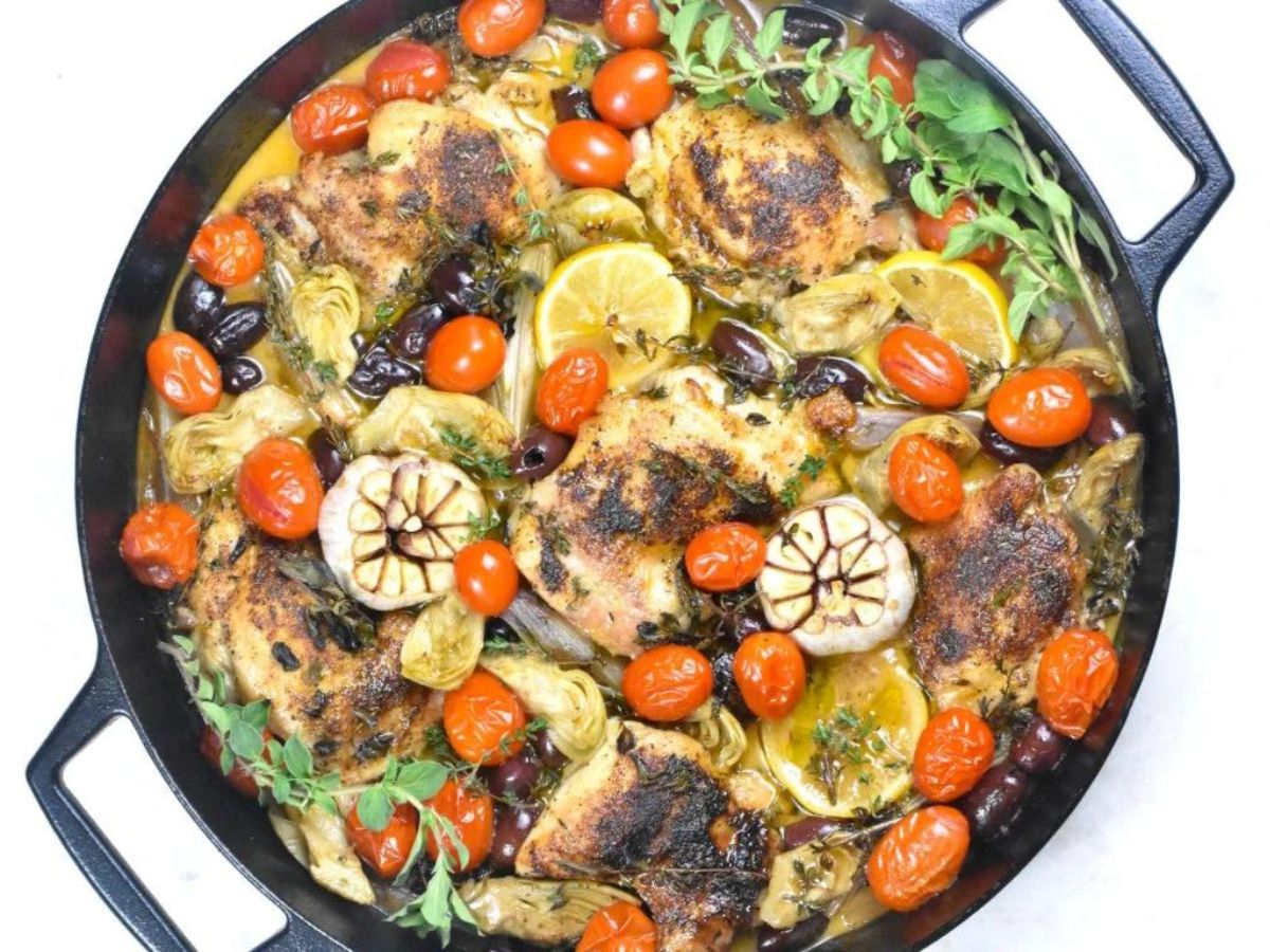 Roasted chicken with tomatoes, lemons, and herbs in a cast iron skillet.
