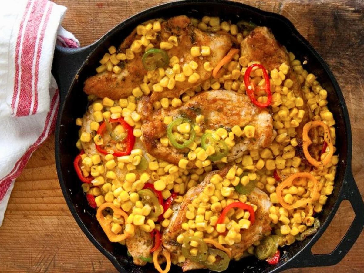 A skillet with chicken thighs and corn garnished with sliced chili peppers.