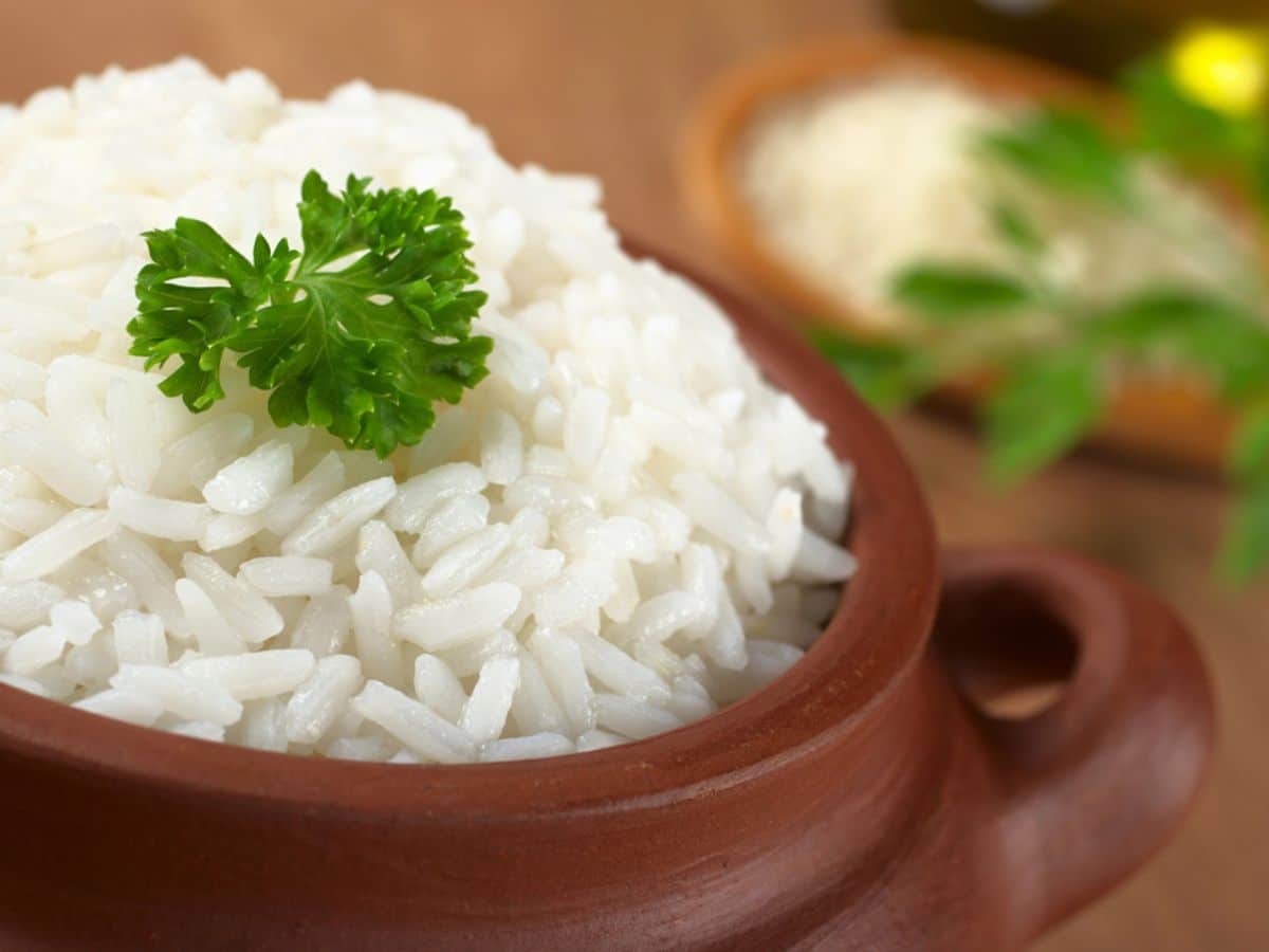 A bowl of cooked white rice garnished with a sprig of parsley.