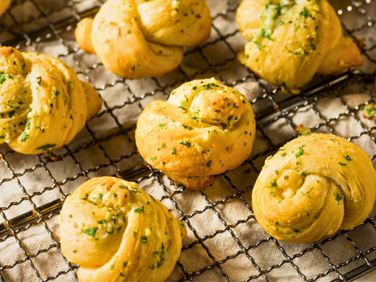 Freshly baked garlic knots sprinkled with herbs on a cooling rack.