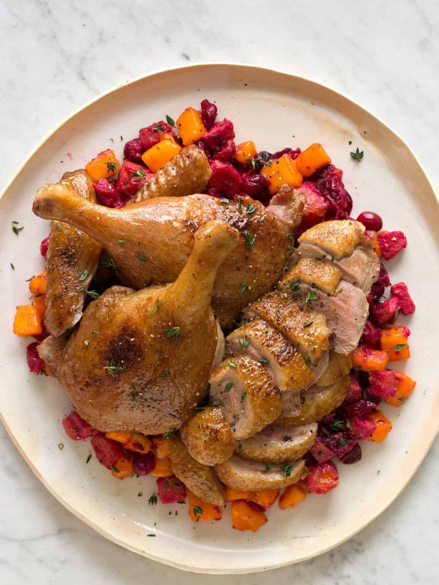 Roasted chicken legs with diced beetroot and carrots served on a beige plate.